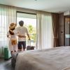 Young couple traveler opening the curtains and looking at the view from the window of a hotel room while on summer vacation, Travel lifestyle concept